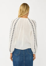 [Color: White/Black] A back facing image of a blonde model wearing a white cotton top with black embroidered details. A classic boho top with a split v-neckline, button front, and long sleeves.  