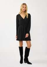 [Color: Black] A front facing image of  a blonde model wearing a black plaid chiffon mini dress with a subtle sheen. Featuring a v-neckline, elastic waist, long sleeves, and a ruffle trimmed hem. A classic black mini with plaid pattern for the holidays. 