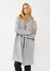 [Color: Platinum] A front facing image of a blonde model wearing a best selling oversized cardigan in a grey blue color. A cozy and thick sweater coat with a hood, an open front, side pockets, a cocoon style silhouette, and a mid length hem. 