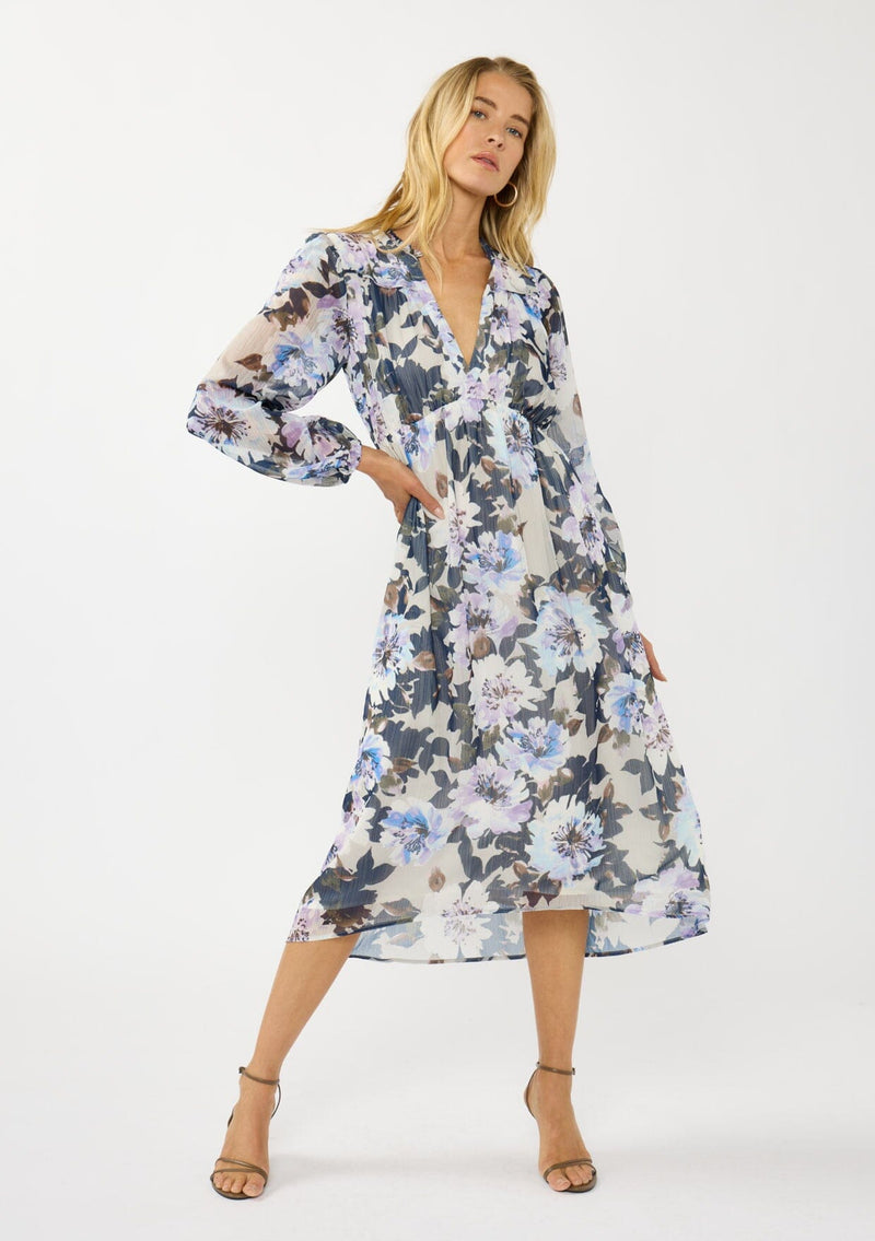 [Color: Grey/Navy] A front facing image of a blonde model wearing a grey and purple floral midi dress with a high-low hemline, empire waist, long sleeves, and a deep v-neckline. Feminine and elegant for weddings and special occasions. 