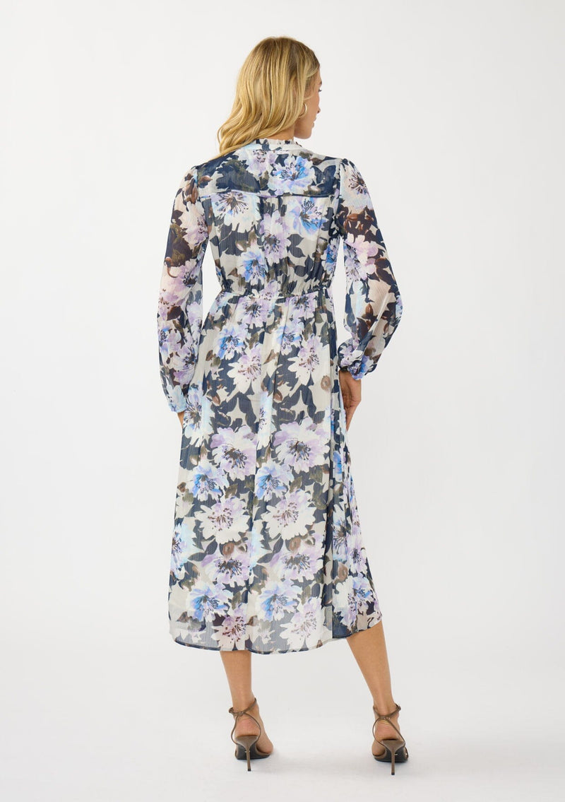 [Color: Grey/Navy] A back facing image of a blonde model wearing a grey and purple floral midi dress with a high-low hemline, empire waist, long sleeves, and a deep v-neckline. Feminine and elegant for weddings and special occasions. 