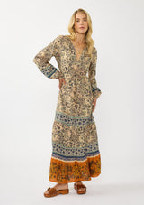 [Color: Natural/Rust] A front facing image of a blonde model wearing a yellow and orange floral border print maxi dress. Featuring long sleeves, a v-neckline, drawstring waist, and a tiered skirt. A fall boho dress for any occasion. 