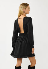 [Color: Black] A back facing image of  a blonde model wearing a black plaid chiffon mini dress with a subtle sheen. Featuring a v-neckline, elastic waist, long sleeves, and a ruffle trimmed hem. A classic black mini with plaid pattern for the holidays. 