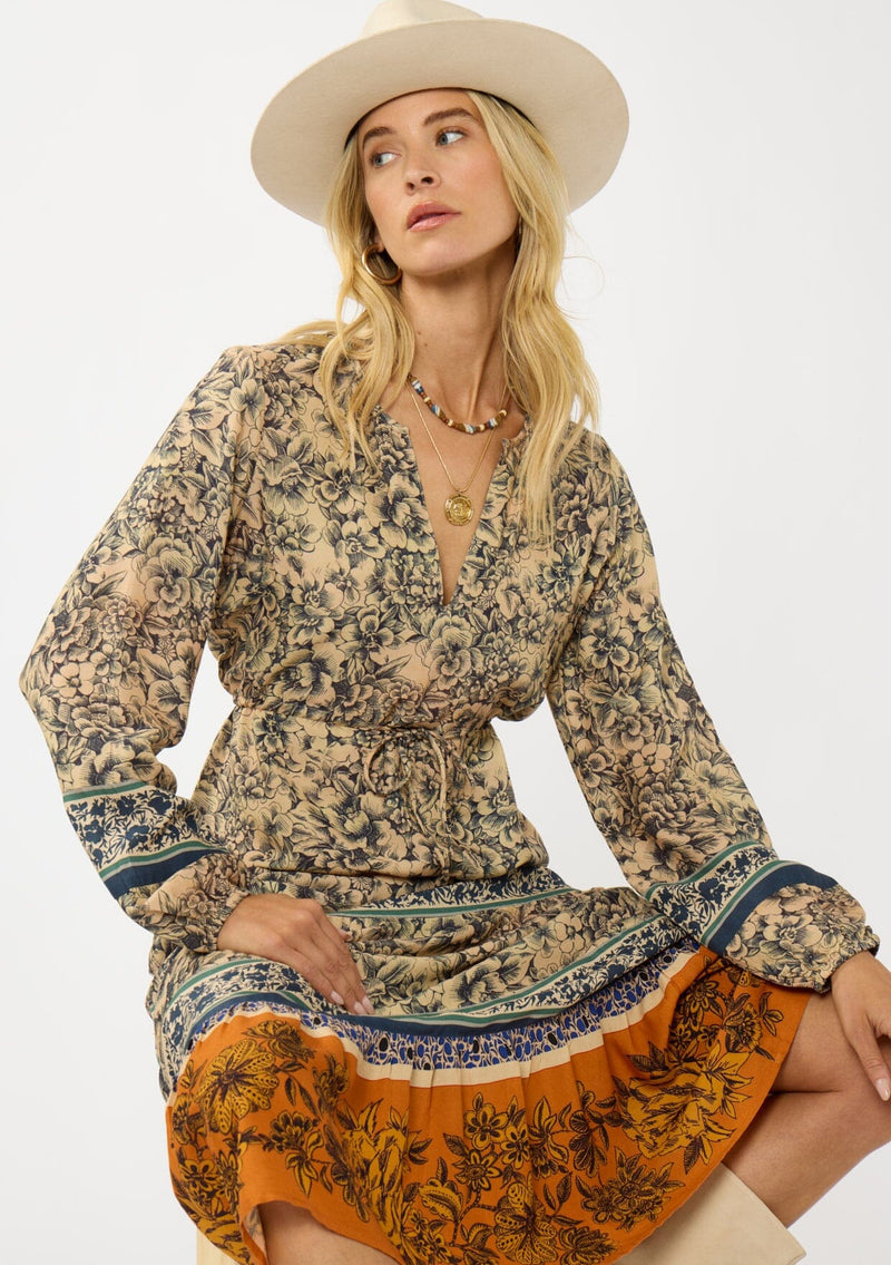 [Color: Natural/Rust] A front facing image of a blonde model wearing a yellow and orange floral border print maxi dress. Featuring long sleeves, a v-neckline, drawstring waist, and a tiered skirt. A fall boho dress for any occasion. 