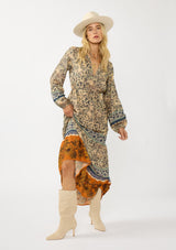 [Color: Natural/Rust] A front facing image of a blonde model wearing a yellow and orange floral border print maxi dress. Featuring long sleeves, a v-neckline, drawstring waist, and a tiered skirt. A fall boho dress for any occasion. 