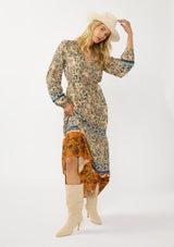 [Color: Natural/Rust] A front facing image of a blonde model wearing a yellow and orange floral border print maxi dress. Featuring long sleeves, a v-neckline, drawstring waist, and a tiered skirt. A fall boho dress for any occasion. 