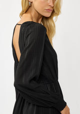 [Color: Black] A detail image of  a blonde model wearing a black plaid chiffon mini dress with a subtle sheen. Featuring a v-neckline, elastic waist, long sleeves, and a ruffle trimmed hem. A classic black mini with plaid pattern for the holidays. 