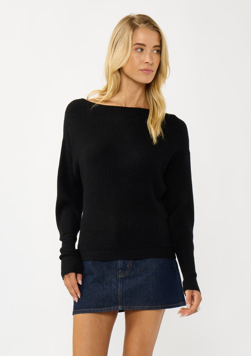 [Color: Black] A front facing image of a blonde model wearing a black waffle knit pullover sweater. With long sleeves, a relaxed fit, and a wide neckline that can be worn off the shoulder.