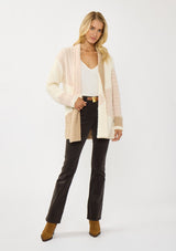 [Color: Natural/Tan] A front facing image of a blonde model wearing a pink and beige cable knit patchwork cardigan with an open front and cozy long sleeves. A cozy layering piece for the fall season. 