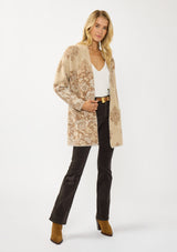 [Color: Sand] A front facing image of a blonde model wearing a brown floral print cardigan with a soft, fuzzy texture featuring an open front and patch pockets. 
