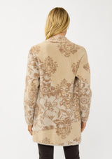 [Color: Sand] A back facing image of a blonde model wearing a brown floral print cardigan with a soft, fuzzy texture featuring an open front and patch pockets. 