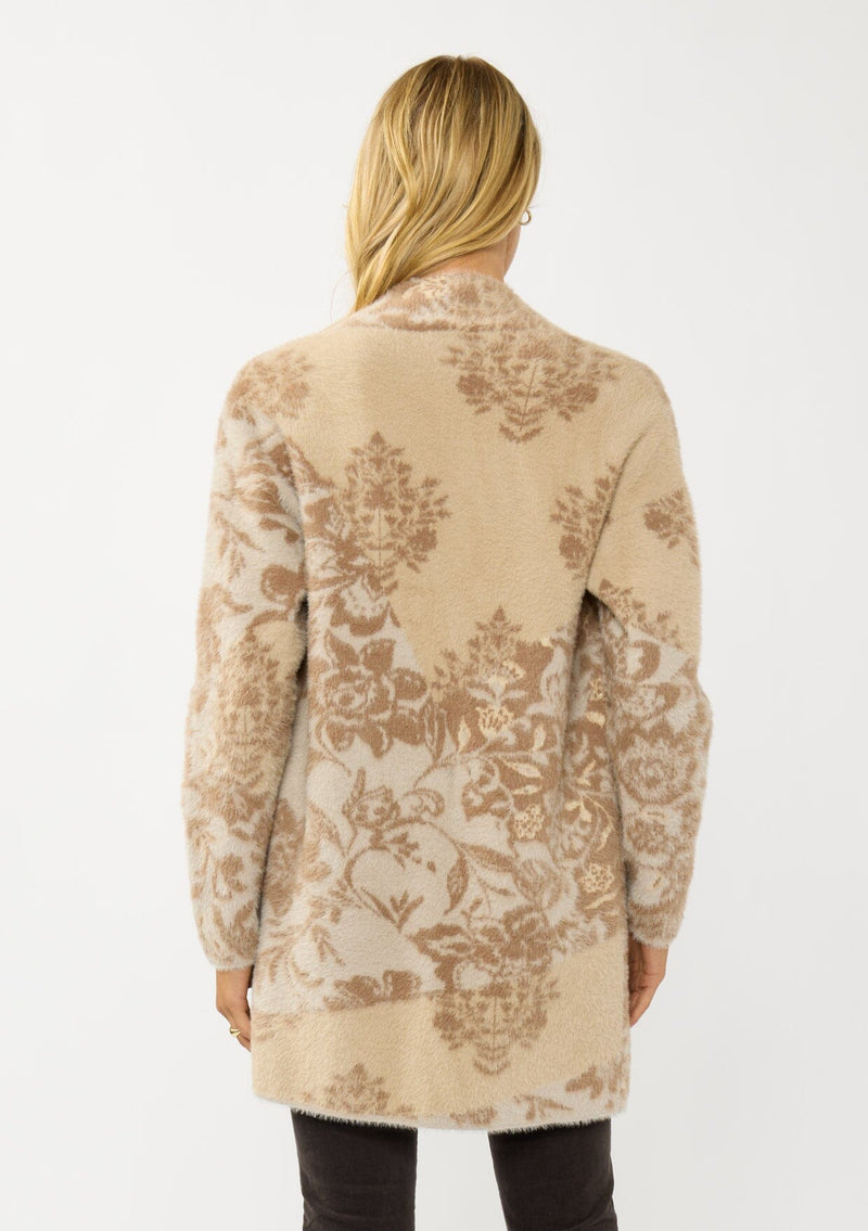 [Color: Sand] A back facing image of a blonde model wearing a brown floral print cardigan with a soft, fuzzy texture featuring an open front and patch pockets. 