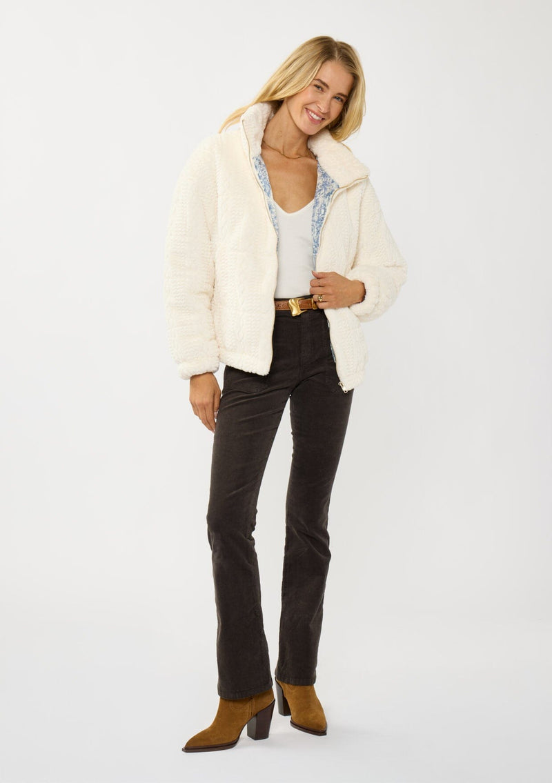 [Color: Cream] A front facing image of a blonde model wearing a plush cream patterned jacket with a zipper front, high collared neckline, contrast lining, and side pockets. A cozy fluffy jacket for the fall and winter season. 