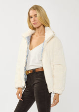 [Color: Cream] A side facing image of a blonde model wearing a plush cream patterned jacket with a zipper front, high collared neckline, contrast lining, and side pockets. A cozy fluffy jacket for the fall and winter season. 