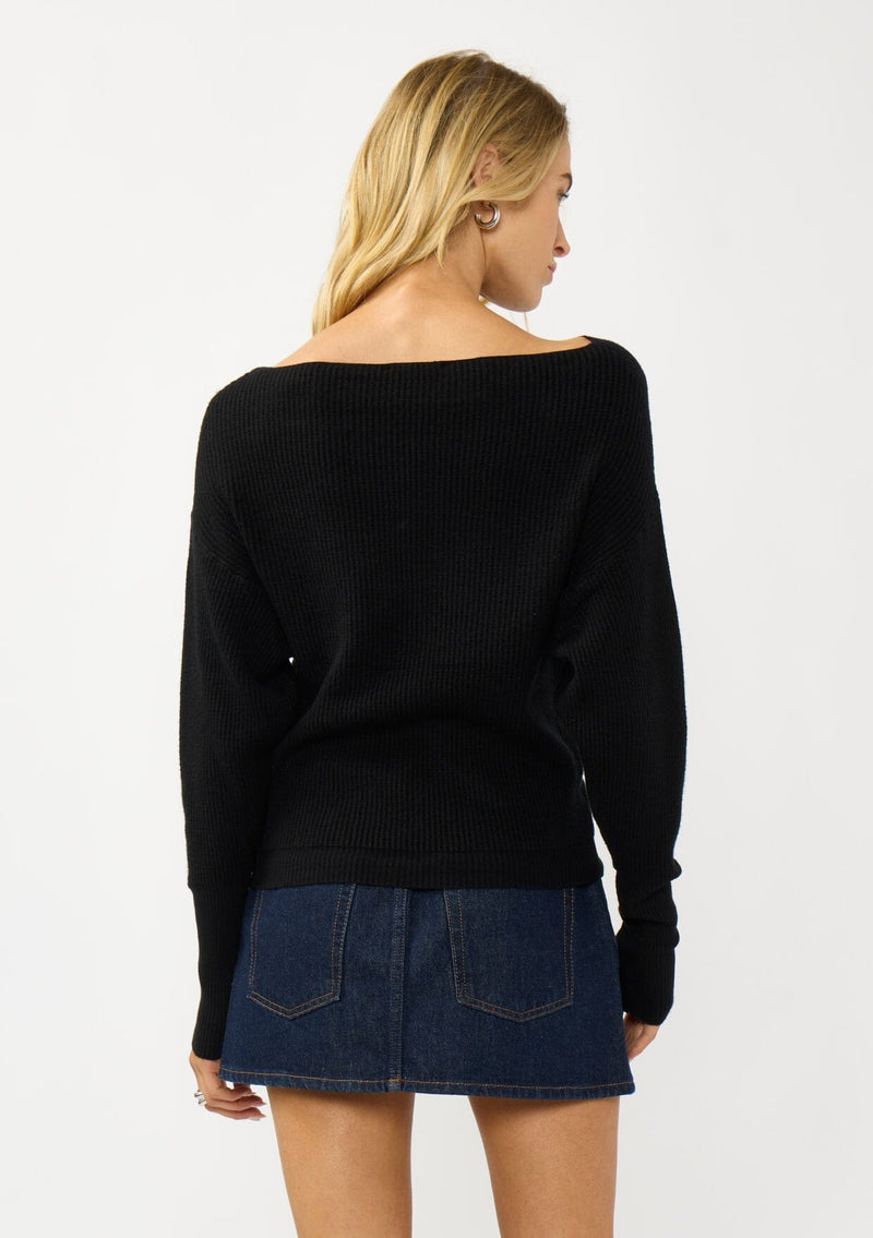 [Color: Black] A back facing image of a blonde model wearing a black waffle knit pullover sweater. With long sleeves, a relaxed fit, and a wide neckline that can be worn off the shoulder.