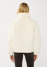 [Color: Cream] A back facing image of a blonde model wearing a plush cream patterned jacket with a zipper front, high collared neckline, contrast lining, and side pockets. A cozy fluffy jacket for the fall and winter season. 