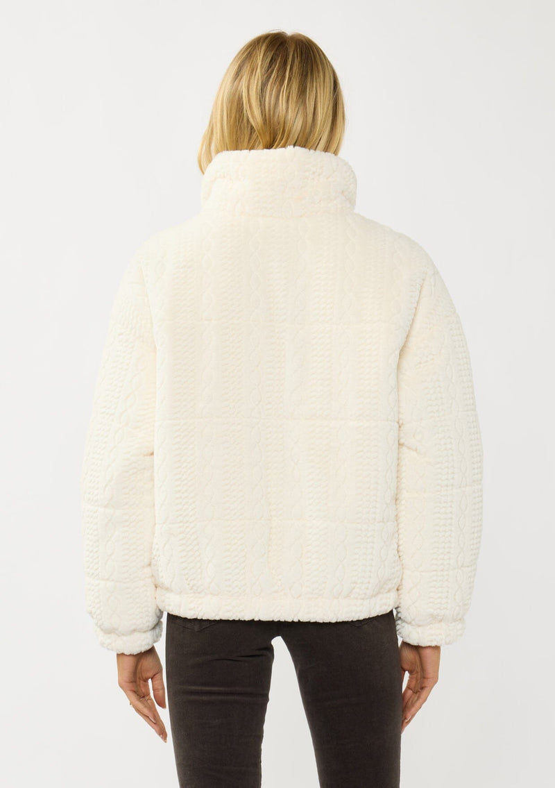 [Color: Cream] A back facing image of a blonde model wearing a plush cream patterned jacket with a zipper front, high collared neckline, contrast lining, and side pockets. A cozy fluffy jacket for the fall and winter season. 