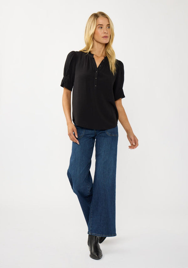 [Color: Black] A front facing image of a blonde model wearing a casual black puff sleeve top with a ruffled neckline, button front, and a gathered sleeve detail. Effortless and versatile for easy layering or wearing on its own. 