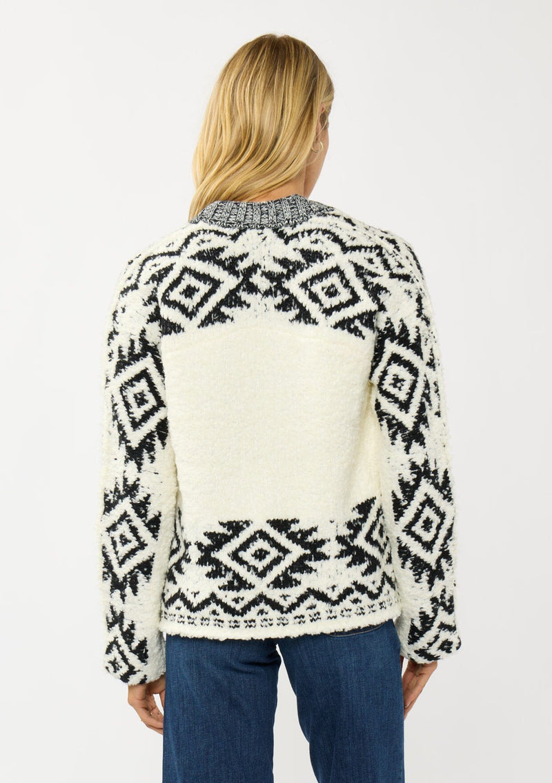[Color: Winter White/Black] A back facing image of a blonde model wearing a white and black tribal pattern sweater jacket with a popcorn texture, button front, and side pockets. A cozy fall sweater for day to night layering. 