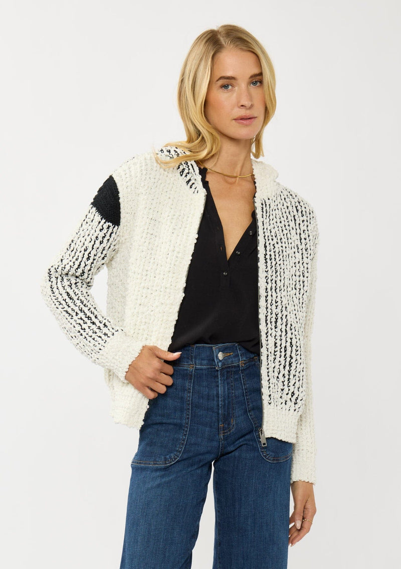 [Color: Cream/Black] A front facing image of a blonde model wearing a color block popcorn sweater jacket. A cozy textured sweater with a zipper front, hoodie, and long sleeves. 