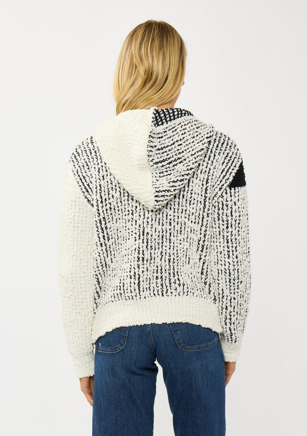 [Color: Cream/Black] A back facing image of a blonde model wearing a color block popcorn sweater jacket. A cozy textured sweater with a zipper front, hoodie, and long sleeves. 
