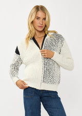 [Color: Cream/Black] A front facing image of a blonde model wearing a color block popcorn sweater jacket. A cozy textured sweater with a zipper front, hoodie, and long sleeves. 