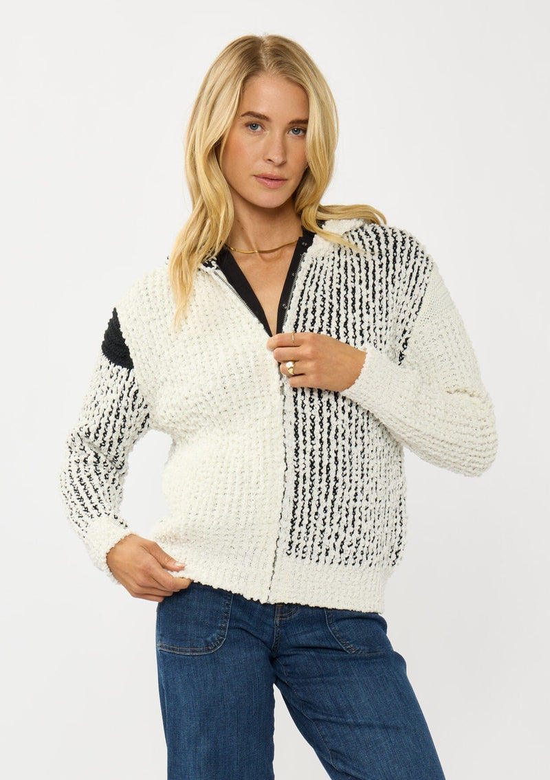 [Color: Cream/Black] A front facing image of a blonde model wearing a color block popcorn sweater jacket. A cozy textured sweater with a zipper front, hoodie, and long sleeves. 