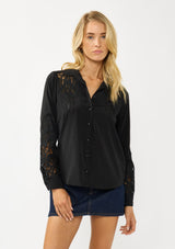 [Color: Black] A front facing image of a blonde model wearing a black shirt with embroidered cutout details on the sleeves and shoulders. Featuring a classic collar neck, button front, and button cuff closure. An elevated fall shirt. 