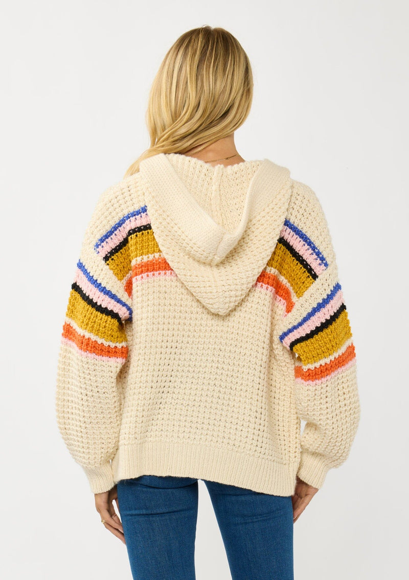 [Color: Natural/Mustard] A back facing image of a blonde model wearing a cream knit cardigan with a colorful striped pattern. Laid back with a hoodie, patch pockets, and button front. A cool girl fall essential!