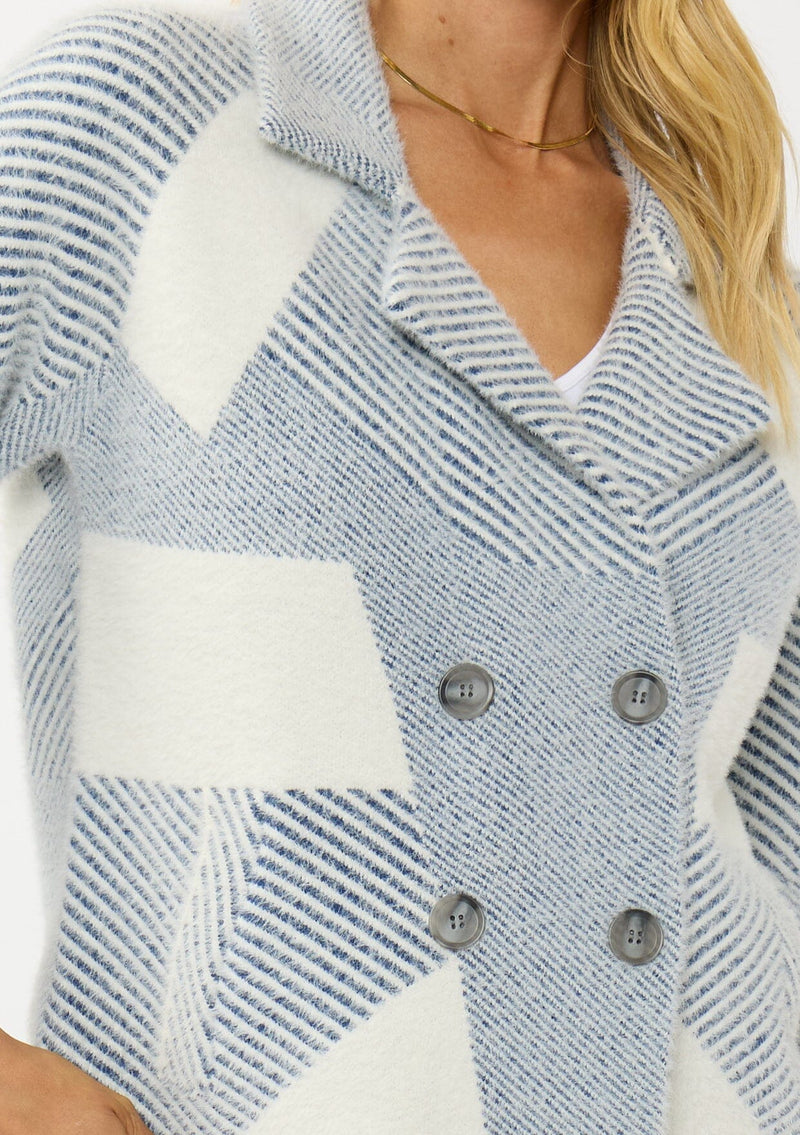 [Color: White/Dusty Blue] A detail image of a blonde model wearing a blue striped sweater jacket with white geometric accents. Featuring a notched lapel, double-breasted front, snap buttons, and side pockets. A cozy and chic fall sweater for the office and casual outings. 