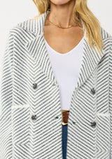 [Color: Black/White] A front facing image of a blonde model wearing a chevron stripe sweater jacket with a soft, fuzzy texture. Featuring a notched collar, double-breasted front, and patch pockets. Cozy and chic for cold weather styling. 
