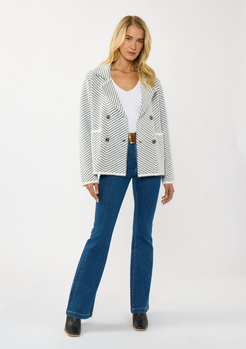 [Color: Black/White] A front facing image of a blonde model wearing a chevron stripe sweater jacket with a soft, fuzzy texture. Featuring a notched collar, double-breasted front, and patch pockets. Cozy and chic for cold weather styling. 