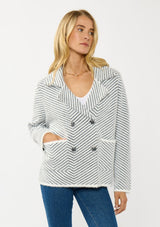 [Color: Black/White] A front facing image of a blonde model wearing a chevron stripe sweater jacket with a soft, fuzzy texture. Featuring a notched collar, double-breasted front, and patch pockets. Cozy and chic for cold weather styling. 
