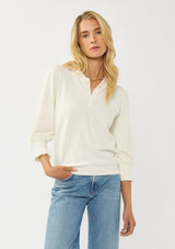 [Color: Cream] A front facing image of a blonde model wearing a cozy sweater top with a button front, long sleeves, and ruffle trim details. Casual and chic for the fall season.