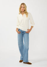 [Color: Cream] A front facing image of a blonde model wearing a cozy sweater top with a button front, long sleeves, and ruffle trim details. Casual and chic for the fall season.