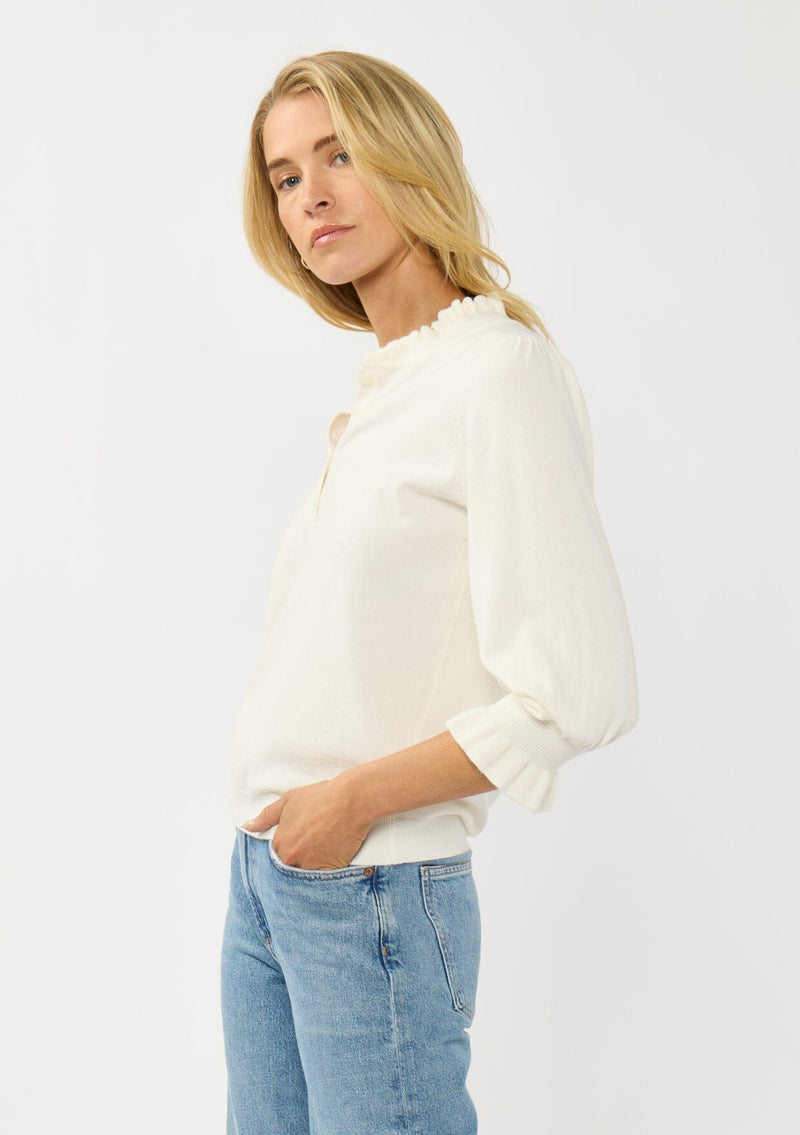 [Color: Cream] A side facing image of a blonde model wearing a cozy sweater top with a button front, long sleeves, and ruffle trim details. Casual and chic for the fall season.