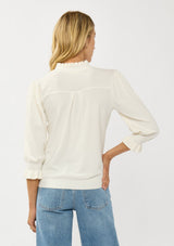 [Color: Cream] A back facing image of a blonde model wearing a cozy sweater top with a button front, long sleeves, and ruffle trim details. Casual and chic for the fall season.
