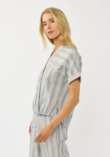 [Color: Grey/White] A side facing image of a blonde model wearing a cotton striped top with a surplice front, short dolman sleeves, and patch pockets. Paired with a matching bottom. 