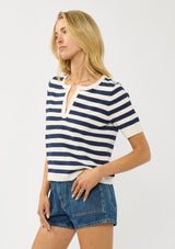 [Color: Cream/Navy] A side facing image of a blonde model wearing a navy striped sweater top with short sleeves and a split v-neckline. A lightweight layer for resort season. 