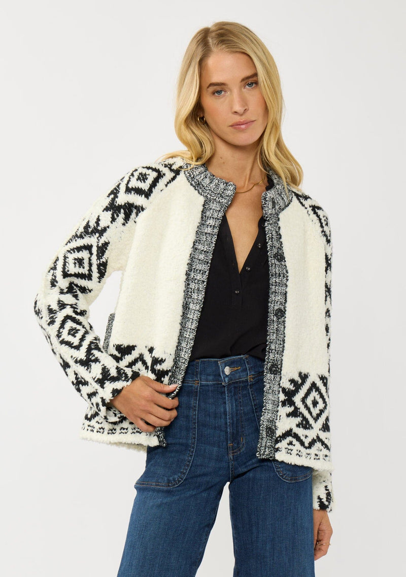 [Color: Winter White/Black] A front facing image of a blonde model wearing a white and black tribal pattern sweater jacket with a popcorn texture, button front, and side pockets. A cozy fall sweater for day to night layering. 