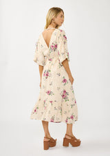 [Color: Natural/Dusty Rose] A side facing image of a blonde model wearing floral jacquard midi dress with a rose floral print. Featuring ruched details, puff sleeves, v-neckline, and a chic open back. A feminine dress for special occasions and holidays. 