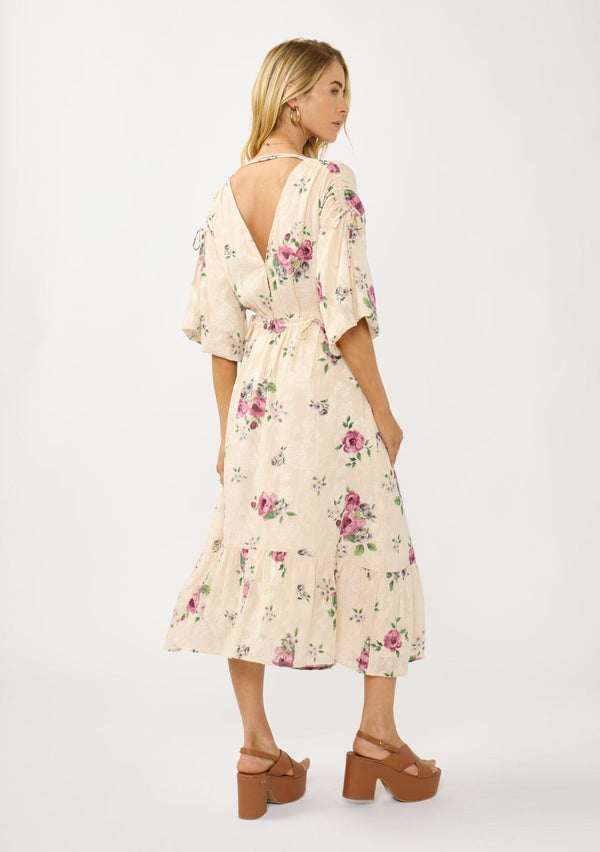 [Color: Natural/Dusty Rose] A side facing image of a blonde model wearing floral jacquard midi dress with a rose floral print. Featuring ruched details, puff sleeves, v-neckline, and a chic open back. A feminine dress for special occasions and holidays. 
