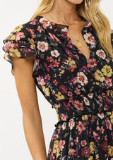 [Color: Black/Rust] A detail image of a blonde model wearing a black floral maxi dress with short flutter sleeves, a split v-neckline, a smocked waist, and side slit. Adorned with ruffle trims, this romantic fall maxi dress is perfect for weddings, holidays, and other special occasions. 