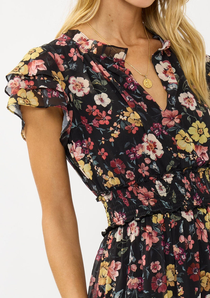 [Color: Black/Rust] A detail image of a blonde model wearing a black floral maxi dress with short flutter sleeves, a split v-neckline, a smocked waist, and side slit. Adorned with ruffle trims, this romantic fall maxi dress is perfect for weddings, holidays, and other special occasions. 