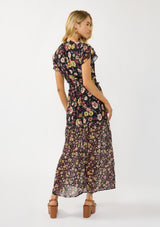 [Color: Black/Rust] A back facing image of a blonde model wearing a black floral maxi dress with short flutter sleeves, a split v-neckline, a smocked waist, and side slit. Adorned with ruffle trims, this romantic fall maxi dress is perfect for weddings, holidays, and other special occasions. 
