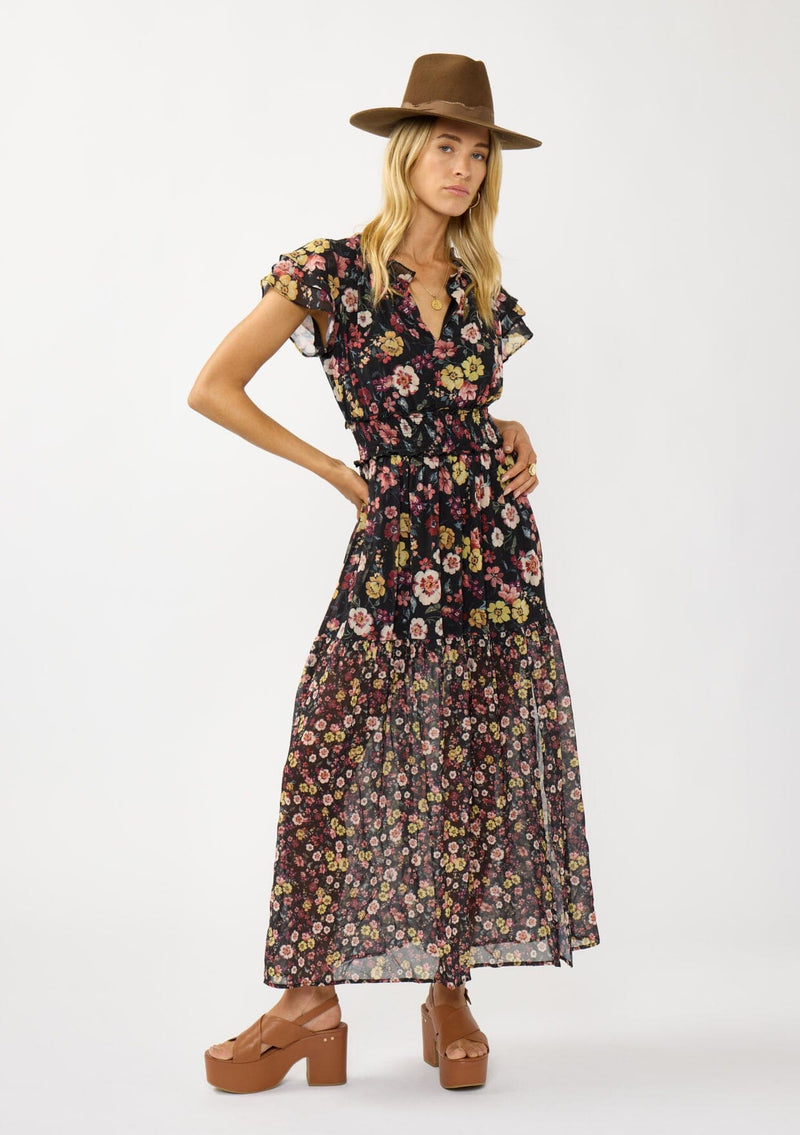 [Color: Black/Rust] A front facing image of a blonde model wearing a black floral maxi dress with short flutter sleeves, a split v-neckline, a smocked waist, and side slit. Adorned with ruffle trims, this romantic fall maxi dress is perfect for weddings, holidays, and other special occasions. 