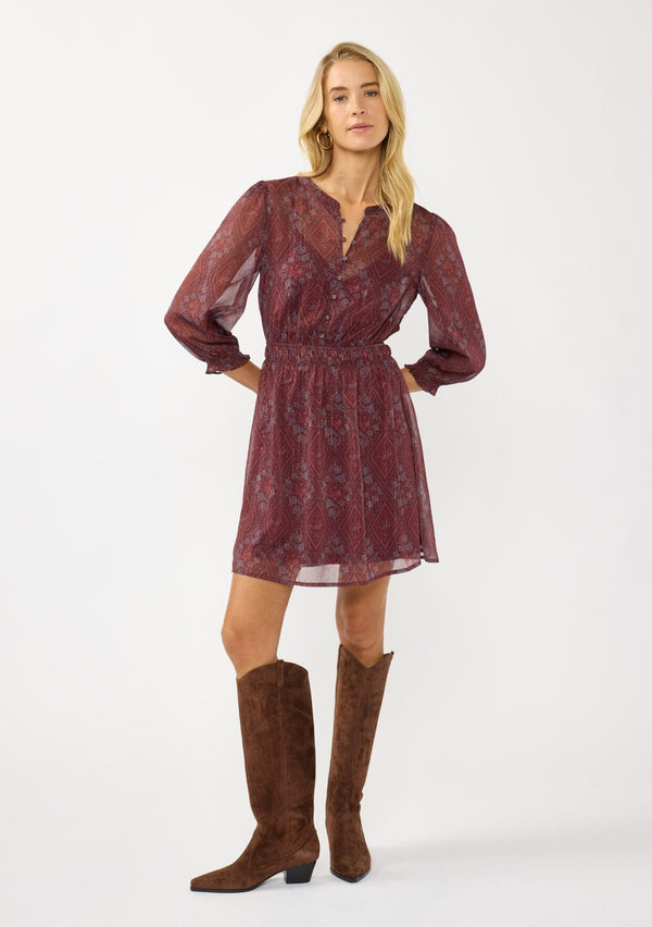[Color: Wine/Rose] A front facing image of a blonde model wearing a floral diamond print chiffon mini dress with metallic thread details, 3/4 sleeves, a button front, and an elastic waist. A special occasion dress for weddings and holidays. 