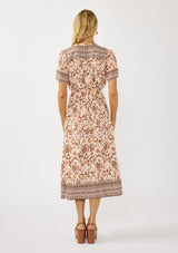 [Color: Natural/Brown] A back facing image of a blonde model wearing a bohemian floral border print mini dress with a split v-neckline, short sleeves, and an elastic waist. 