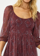 [Color: Wine/Rose] A detail image of a blonde model wearing a floral diamond print chiffon maxi dress with metallic threads, a tie back, 3/4 sleeves, and a scoop neckline. A flattering special occasion dress for weddings or holidays. 