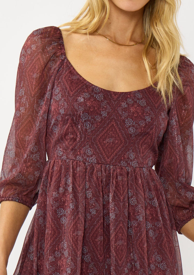 [Color: Wine/Rose] A detail image of a blonde model wearing a floral diamond print chiffon maxi dress with metallic threads, a tie back, 3/4 sleeves, and a scoop neckline. A flattering special occasion dress for weddings or holidays. 